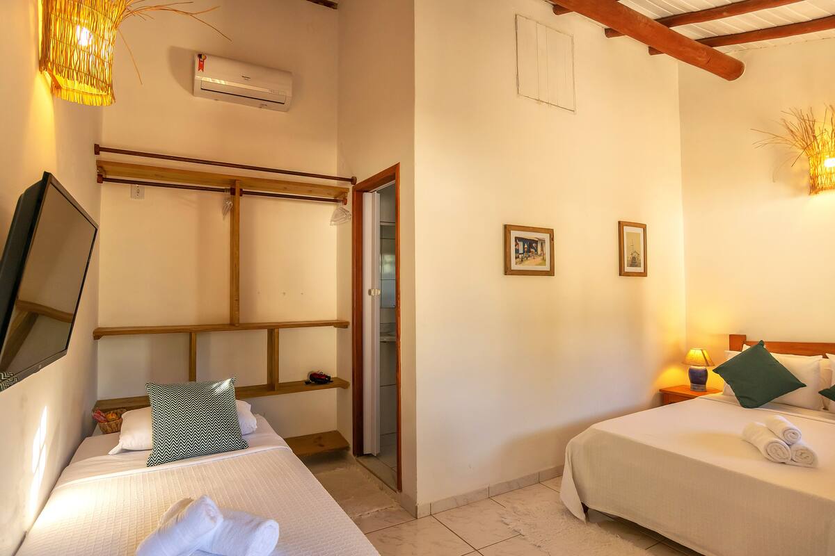 Ein Hotelzimmer mit zwei Betten, einem Holz-Kopfteil, einem Flachbildfernseher, einer fest installierten Klimaanlage und einem kleinen Nachttisch mit Lampe.
