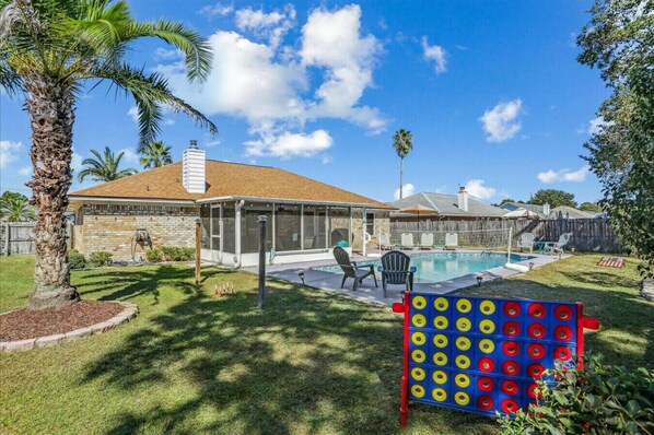A backyard with a swimming pool, a covered patio, and a lawn.