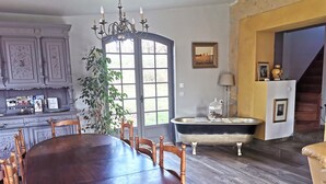 Zona pranzo con un grande tavolo in legno e sedie, un lampadario, una vasca da bagno d'epoca e una pianta.