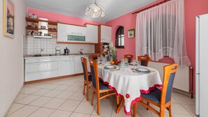 Un comedor con una mesa dispuesta para cuatro personas, rodeada de sillas de madera con cojines azules. Una servilleta blanca con borde rojo cubre la mesa.