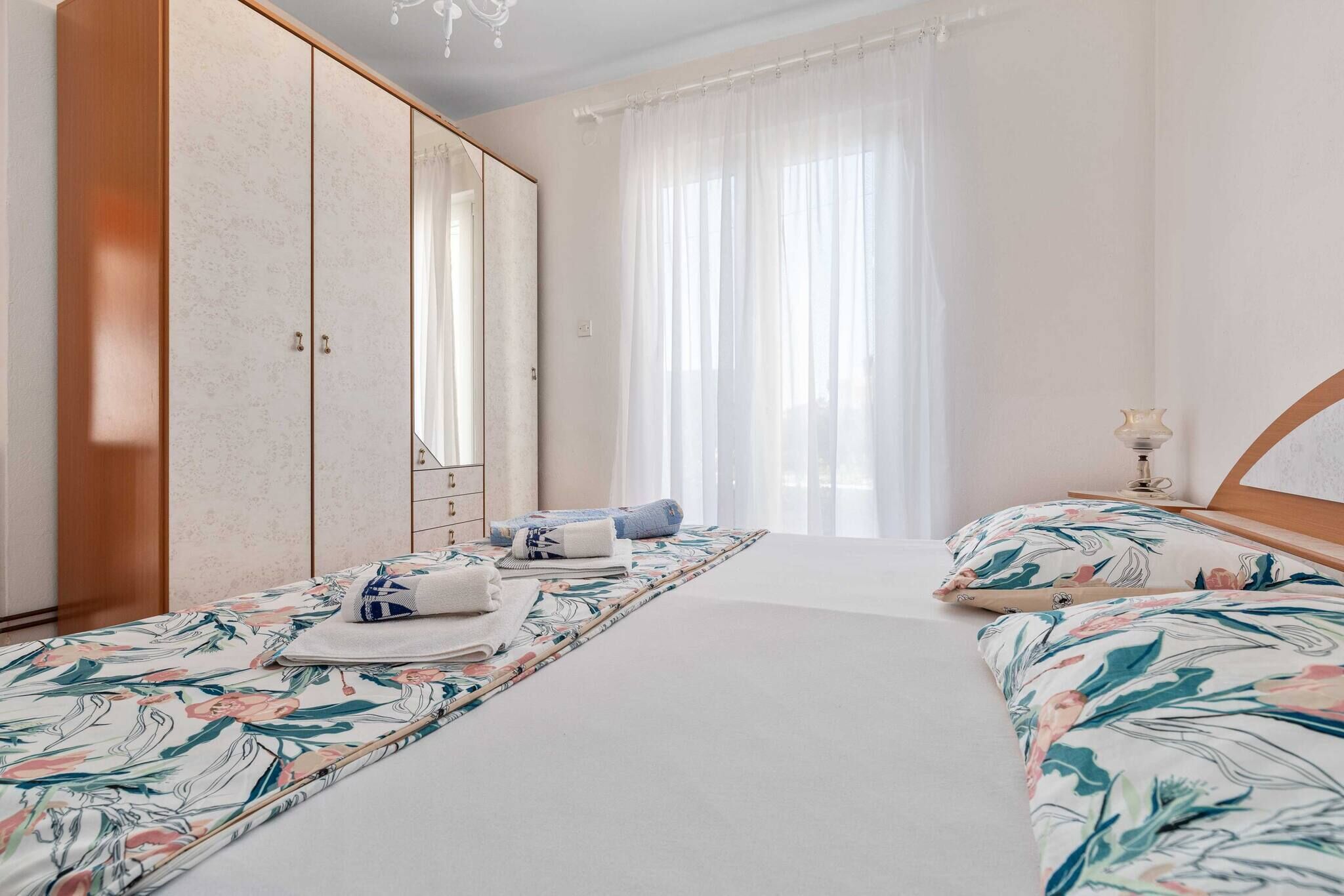 A hotel room with a large bed, a wardrobe, a bedside table, and a window with curtains.