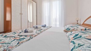 Habitación de hotel con una cama grande, un armario, una mesita de noche y una ventana con cortinas.