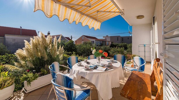 Un patio al aire libre con una mesa redonda, sillas y un toldo a rayas.
