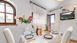 Ein Essbereich mit einem Tisch für vier Personen, weißen Stühlen, einer Blumenvase, einer Obstschale und einem Gemälde an der Wand.