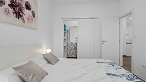 Un dormitori amb un llit, una tauleta de nit, una làmpada penjada a la paret i una porta que dóna a un bany.