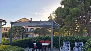 Una zona de pati coberta amb una taula i cadires, envoltada de vegetació i un arbust.