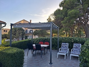 Un'area patio coperta con tavolo e sedie, immersa nel verde e circondata da un siepe.
