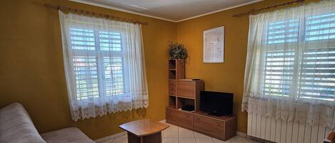 Een woonkamer met een bank, een bijzettafeltje, een tv-meubel en een potplant.