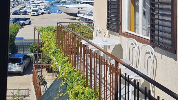 Un balcon donnant sur une marina, une table et des chaises blanches, et une balustrade.