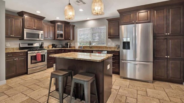A modern kitchen with dark wood cabinets, stainless steel appliances, and a central island with stools. - Renovated Retreat | Spa + Sauna | Near Downtown (Prescott)