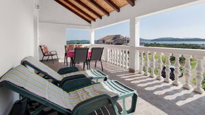 Un espace extérieur abrité, doté de chaises longues et d’une table, offrant une vue panoramique sur un lac et des collines lointaines.