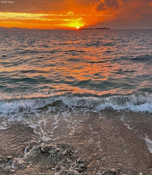 A beach with waves at sunset, a clear sky, and distant land.