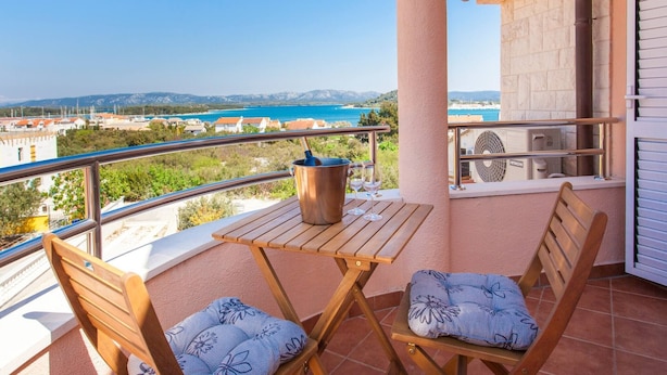 A balcony with a table, two chairs, a bucket, and a fan.