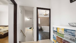 A modern hotel room with a bed, a bathroom with a bathtub, and a colorful wall art piece.