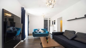 A modern living room with a blue sofa, a black sofa, a wooden coffee table, and a flat-screen TV mounted on the wall.