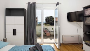 A modern bedroom with a bed, a TV, a heater, and a sliding glass door to a balcony.