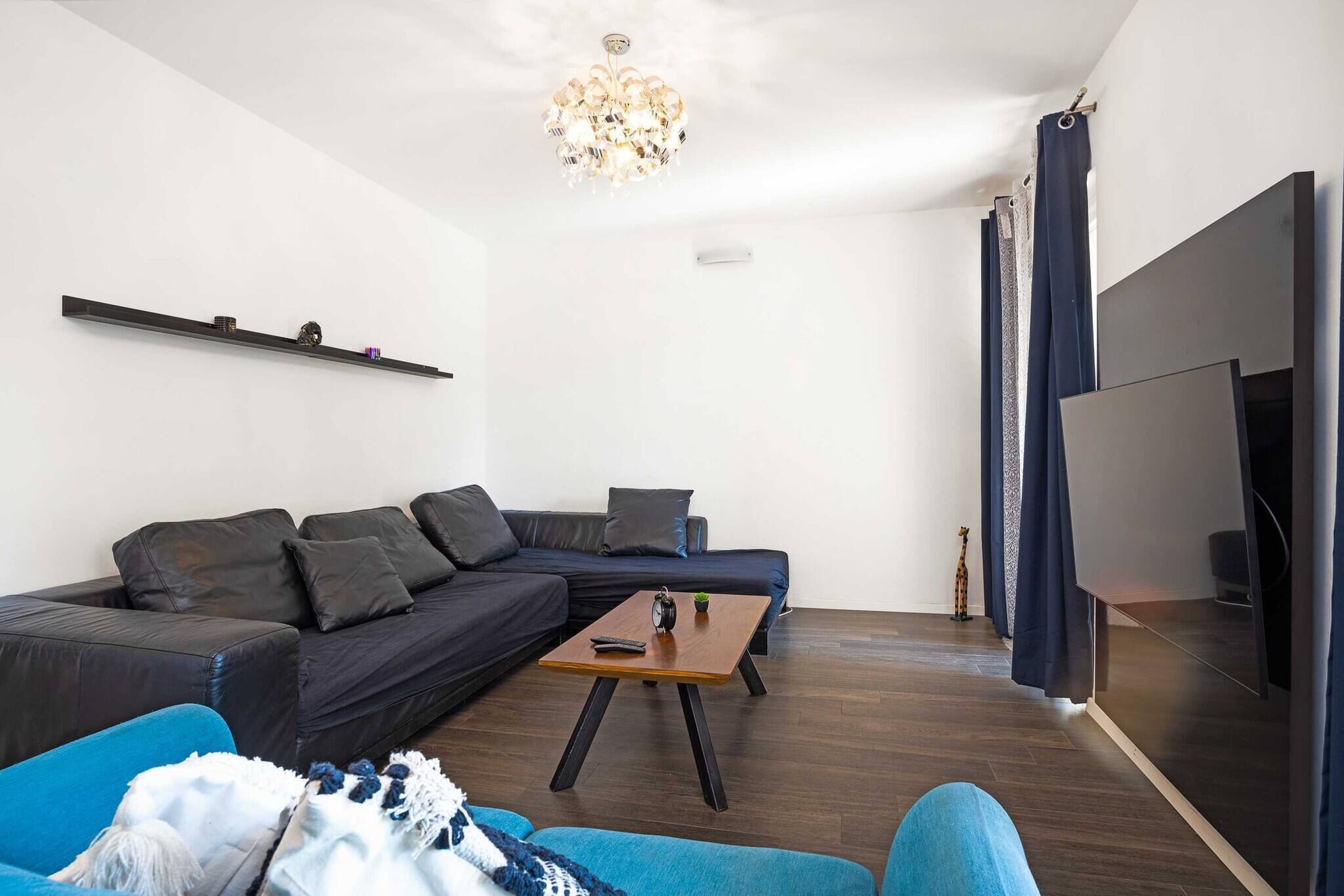 Uma sala de estar moderna com um sofá seccional, uma mesinha de centro, uma televisão e um lustre.