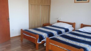 Une chambre avec deux lits en bois, une armoire et un tableau encadré au mur.