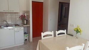 Une cuisine avec des meubles blancs, un évier et une cuisinière. On y trouve une table à manger avec des chaises et un vase rempli de fleurs.