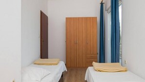 Une petite chambre propre, avec deux lits simples, une armoire en bois et une fenêtre ornée de rideaux bleus.