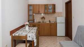 Une cuisine de taille réduite, avec des meubles en bois, un réfrigérateur blanc et une table à manger recouverte d’une nappe à motifs.