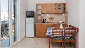 A compact kitchen with wooden cabinets, a small refrigerator, a television, and a dining table with chairs. - Apartments Gaj Brodarica - A9 (Šibenik-Brodarica)