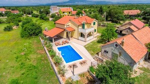 A large house with a swimming pool, surrounded by lush greenery and a mountainous backdrop.