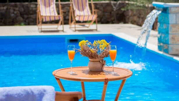 A poolside setting with a table, two chairs, and a vase of flowers.