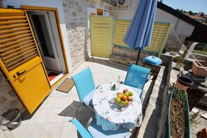 Um pátio externo com uma mesa posta para dois, uma porta amarela e um guarda-sol azul.
