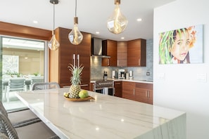 Una cocina moderna con una isla de mármol, armarios de madera e iluminación colgante.