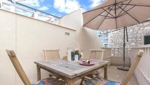 An outdoor patio with a wooden table and chairs, a white birdcage, and a pink plate with food. - Stone Apartment Primosten (Primošten)