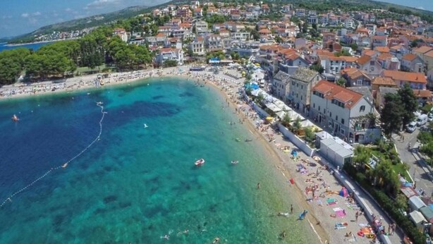 An aerial view of a coastal town with a beach, clear blue waters, and buildings along the shore. - Stone Apartment Primosten (Primošten)