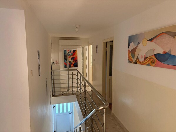 Un couloir avec un escalier, une porte au fond et une peinture abstraite aux couleurs vives accrochée au mur.