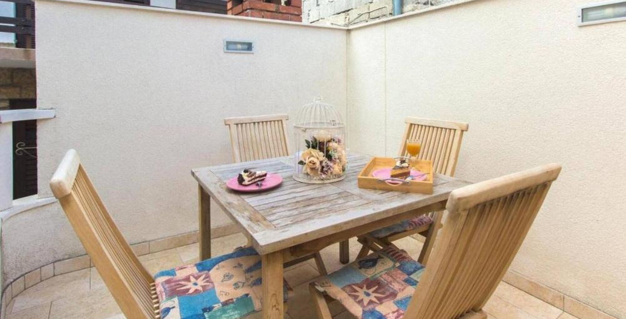 Una mesa de madera con sillas, una jaula de pájaros de cristal con flores y una bandeja con comida y bebida.