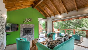A living room with green walls, a fireplace, and a large window overlooking a deck.