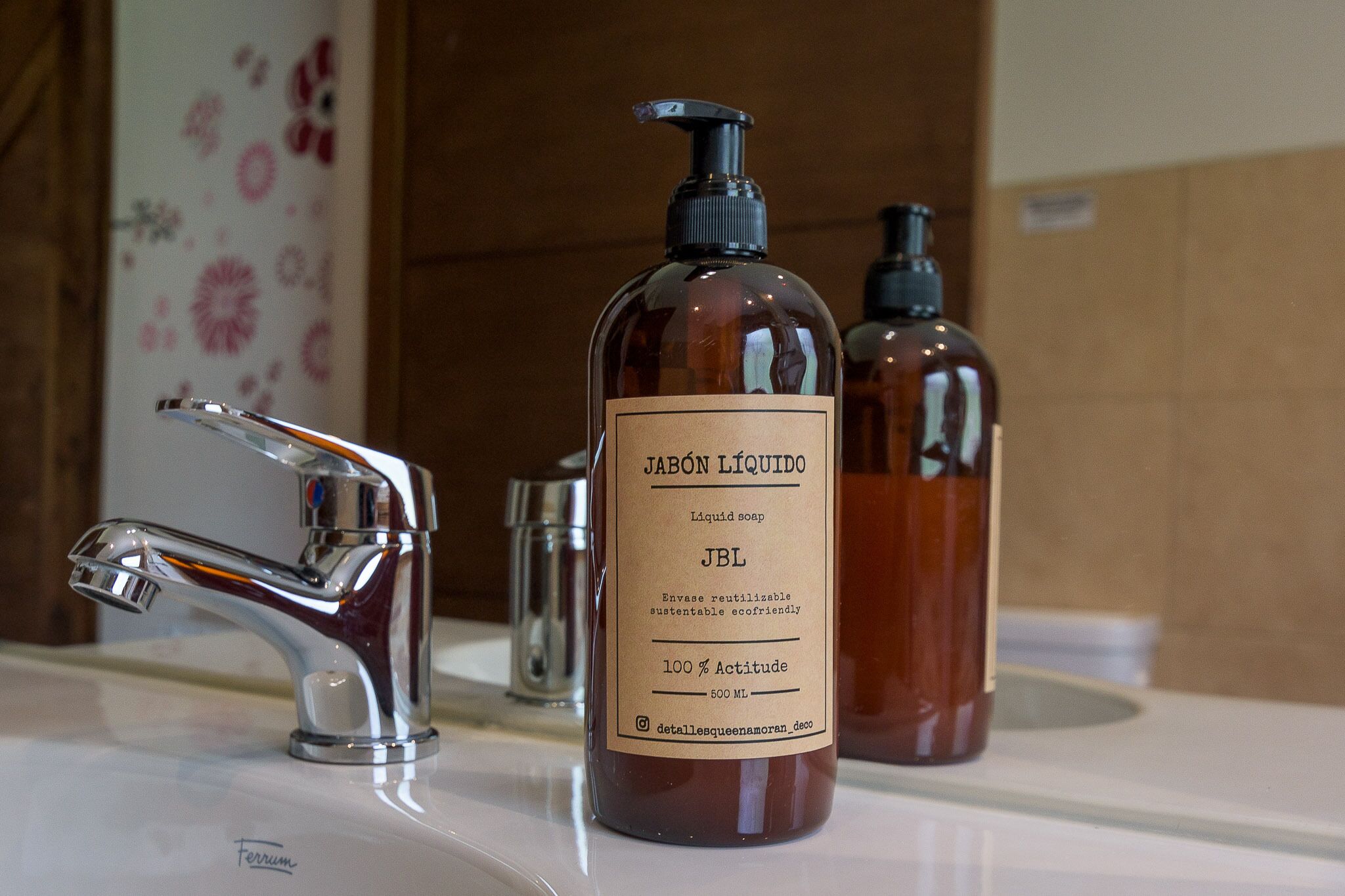 A bathroom with a chrome faucet, a bottle of liquid soap labeled 'JABÓN LÍQUIDO JBL', and a smaller bottle in the background.
