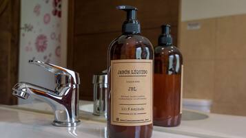 A bathroom with a chrome faucet, a bottle of liquid soap labeled 'JABÓN LÍQUIDO JBL', and a smaller bottle in the background.