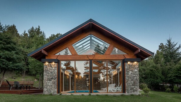 A modern house with a stone exterior, large glass windows, and a wooden roof. - Solar Selvana - Casas de montaña (Villa La Angostura)
