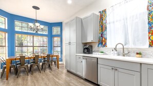 Une cuisine moderne avec des meubles de couleur gris clair, un plan de travail blanc et un coin repas comprenant une table en bois et des chaises en métal.