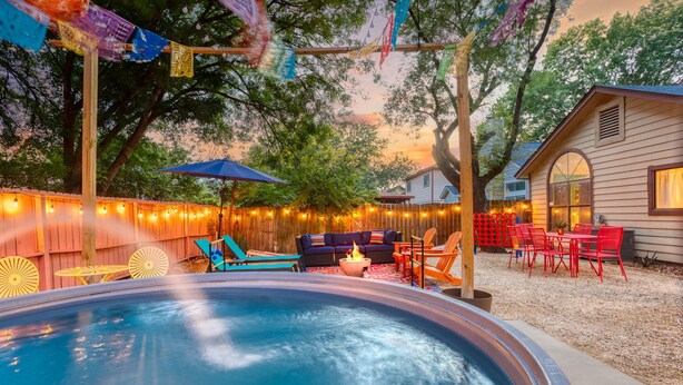 Un jardin avec un jacuzzi, du mobilier d’extérieur, des guirlandes lumineuses et une clôture en bois.