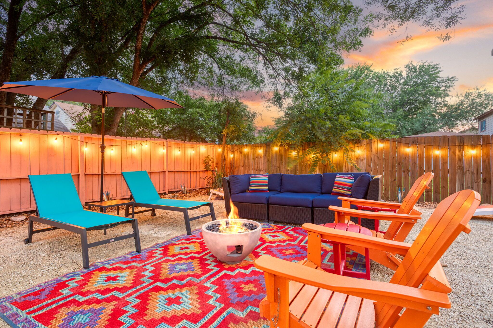 Eine Terrasse im Freien mit Feuerstelle, Liegestühlen, einer Couch und Lichterketten.