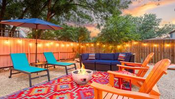 Eine Terrasse im Freien mit Feuerstelle, Liegestühlen, einer Couch und Lichterketten.