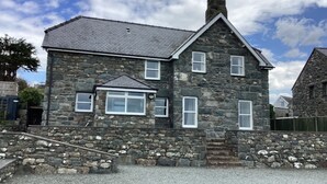 A stone house with a gabled roof, multiple windows, and a chimney. - Traditional Welsh cottage in the village of Dyffryn Ardudwy (Dyffryn Ardudwy)