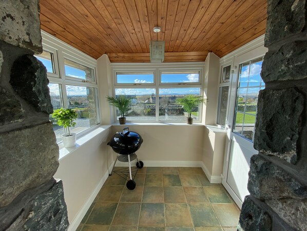 A room with a stone wall, a wooden ceiling, and a view of a rural landscape through large windows.