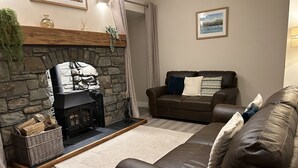 A cozy living room with a stone fireplace, a brown leather sofa, and a wooden coffee table. - Traditional Welsh cottage in the village of Dyffryn Ardudwy (Dyffryn Ardudwy)