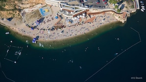 An aerial view of a coastal area with a beach, a promenade, and a building with a modern design.