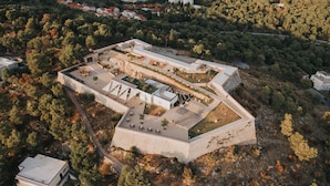 An aerial view of a fortified complex with multiple buildings, pathways, and surrounding forested area.