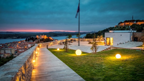 A waterfront property with a wooden deck, a flagpole, and a modern building with glass doors.
