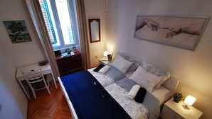A bedroom with a bed, bedside tables, a desk, and a window.
