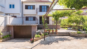 A residential building with a gated entrance, a balcony, and a garden area with potted plants.